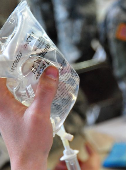 A hand holding an intravenous bag of normal saline in a medical clinic.